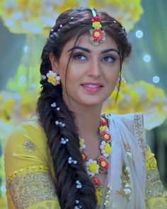 a woman with braids and flowers in her hair smiling at the camera while wearing a yellow outfit