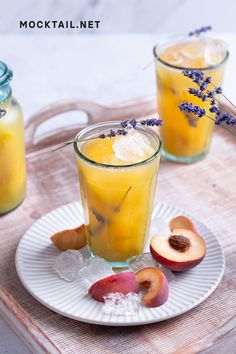 two glasses filled with liquid sitting on top of a white plate next to sliced peaches