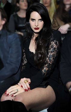 a woman with long black hair and red nails sitting in front of a group of people