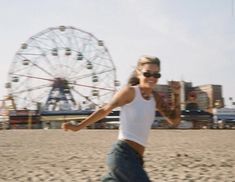 a woman is running on the beach with a ferris wheel in the backgroud