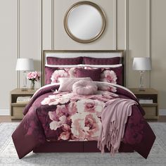 a bed with purple and pink floral comforter set in a white room next to a round mirror