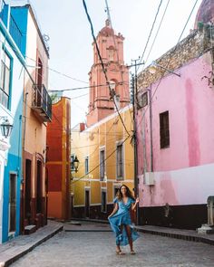 a woman in a blue dress is walking through an alleyway with colorful buildings on both sides