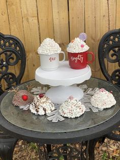 two mugs are sitting on top of a table with cupcakes and marshmallows