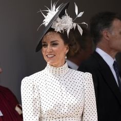 a woman in a white dress and black hat smiles as she stands next to other people