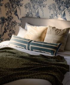 a bed with blue and white wallpaper, pillows and blankets on top of it