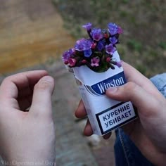 a person holding a tube with purple flowers in it and a sticker on the end