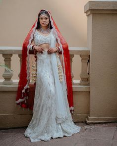 a woman in a white and red bridal gown posing for the camera with her veil draped over her head