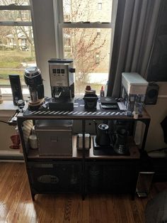 there is a coffee maker on top of the table in front of a window with curtains