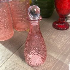 a pink glass bottle sitting on top of a wooden table next to other vases