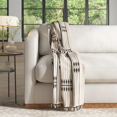 a white couch sitting next to a table with a lamp and window in the background