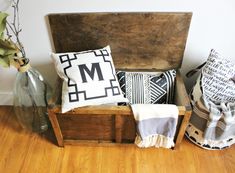 a wooden box filled with pillows on top of a hard wood floor next to a vase