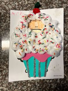 a cupcake decorated with sprinkles and frosting on top of a piece of paper