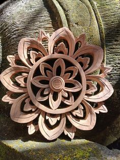 a carved wooden flower sitting on top of a stone wall next to moss covered rocks