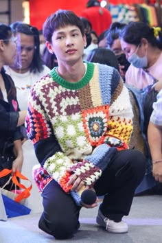 a young man sitting on the floor in front of a group of people wearing sweaters