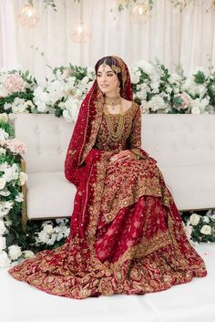 a woman sitting on top of a white couch wearing a red and gold wedding dress