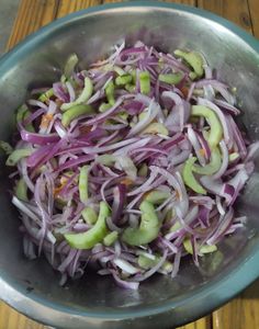 a metal bowl filled with red onions and cucumber slices on top of a wooden table