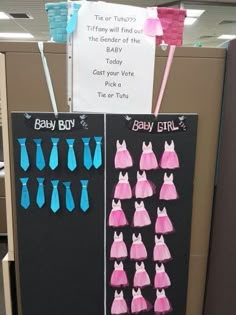 an office cubicle decorated with pink and blue baby dresses on black board, hanging from the ceiling