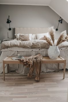 a white vase sitting on top of a wooden table next to a bed in a bedroom