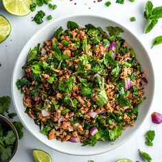 a white bowl filled with meat and veggies next to sliced limes on the side