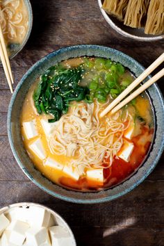 a bowl filled with noodles, tofu and spinach on top of a wooden table