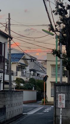 an empty street with power lines above it and houses in the background at sunset or dawn