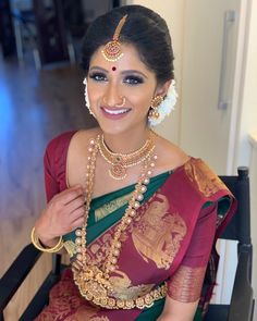 a woman in a red and green sari with gold jewelry on her neck smiling