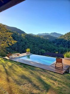 a wooden deck next to a swimming pool surrounded by lush green trees and mountains in the distance