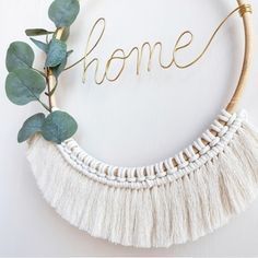 the word home written in gold lettering on a white wall with greenery and leaves