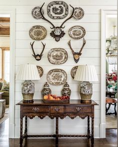 a table with two lamps and plates on it in front of a wall mounted deer head