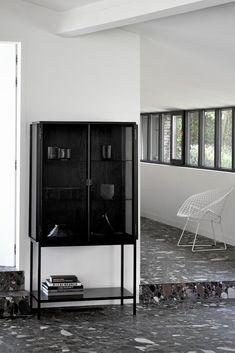 a black cabinet sitting in the middle of a living room next to a white chair