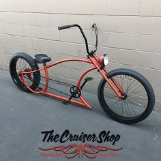 an orange tricycle parked in front of a brick wall with the cruiser shop logo on it