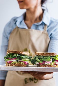 a woman holding a tray with two sandwiches on it