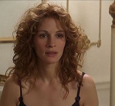 a woman with curly hair is looking at the camera while standing in front of a mirror