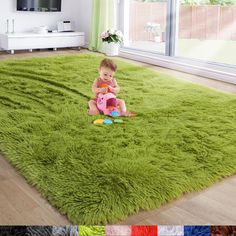 a baby sitting on top of a green rug in front of a window with windows