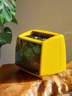 a yellow television sitting on top of a wooden table next to a potted plant