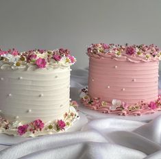 two cakes decorated with pink and white frosting are sitting on a table covered in satin material