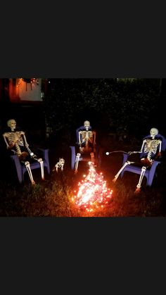 three skeletons sitting in lawn chairs around a campfire