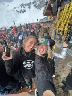 two women taking a selfie at the bottom of a ski slope in front of a crowd