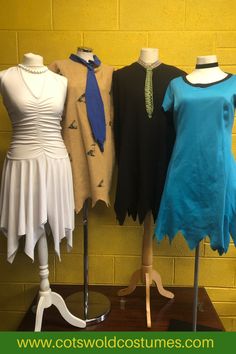 three mannequins dressed in different styles of clothing on display against a yellow brick wall