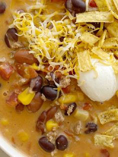 a white bowl filled with black beans, corn and tortilla chips next to sour cream