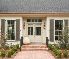 a white house with green shutters and brick walkway