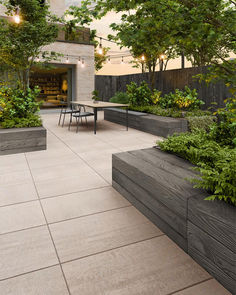 an outdoor dining area with benches and tables surrounded by trees, shrubs and plants on the side