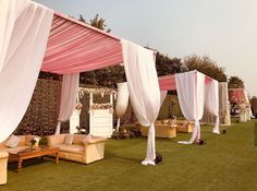 an outdoor wedding setup with white draping and couches on the grass area