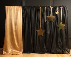 three gold stars are hanging on black curtains