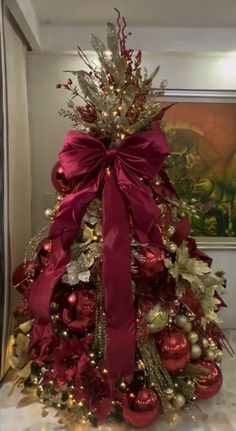 a decorated christmas tree with red and gold ornaments on the top, in front of a painting