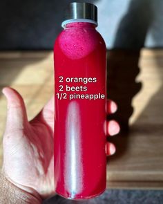 a hand holding a pink water bottle with 2 oranges and 1 beets in it