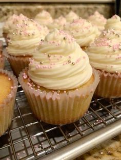 cupcakes with white frosting and pink sprinkles on a cooling rack