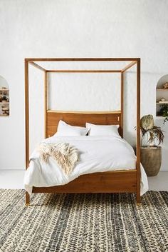 a bed with white sheets and pillows in a room next to a potted plant