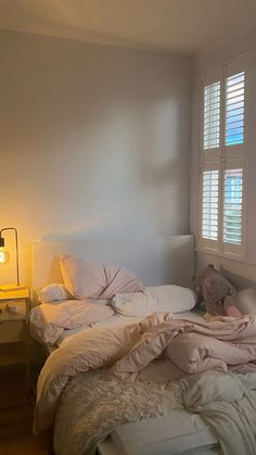 an unmade bed with white sheets and pillows in a bedroom next to a window