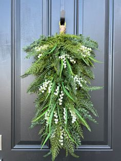 a wreath hanging on the front door of a house decorated with white flowers and greenery